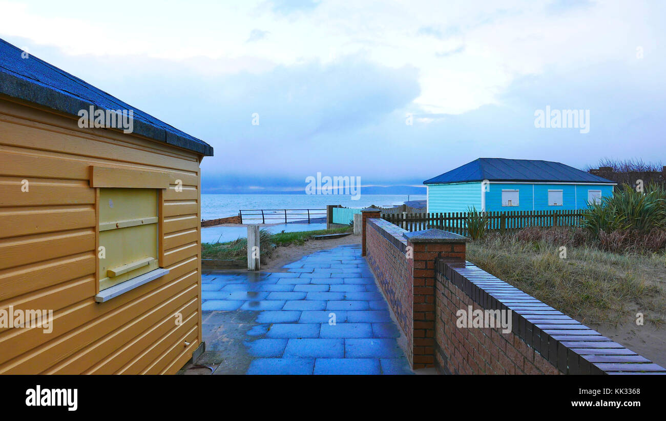 Chiuso fino cabine sulla spiaggia, in un freddo giorno di inverni al tramonto su Fleetwood fronte mare con pioggia in arrivo sul lontano orizzonte Foto Stock