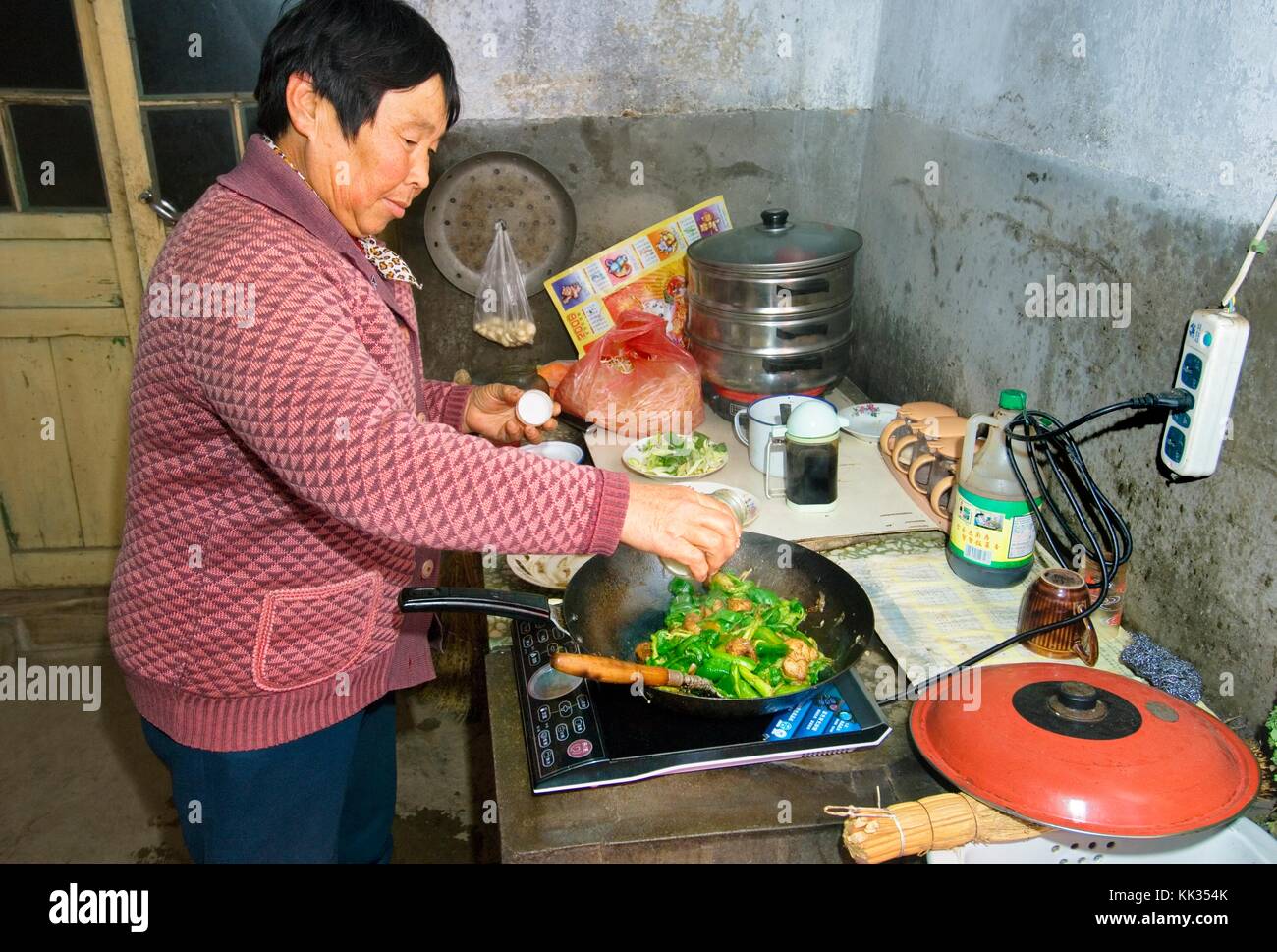 La moglie di un agricoltore di cottura Farina vegetale sul piano di cottura elettrico in una fattoria di cucina nel borgo di poli vicino Penglai, Provincia di Shandong, Cina Foto Stock
