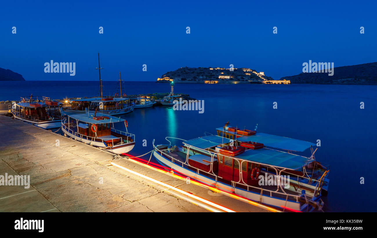Turistiche e barche da pesca al molo del villaggio di Plaka, vicino all'isola di Spinalonga di notte, Creta, Grecia Foto Stock