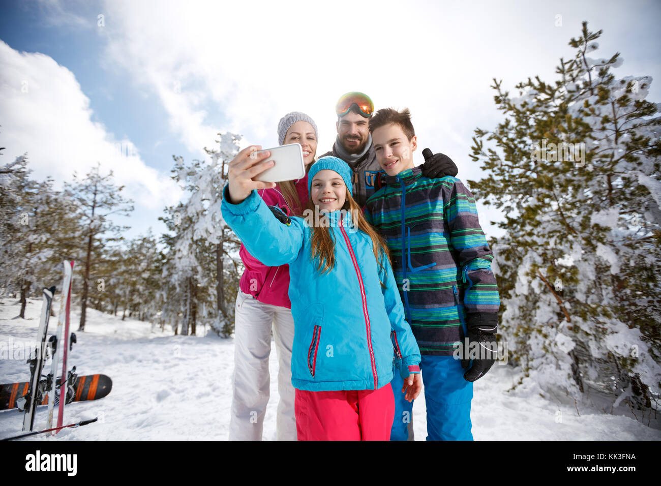 Ragazza con la famiglia su sci prendendo foto con il telefono cellulare Foto Stock