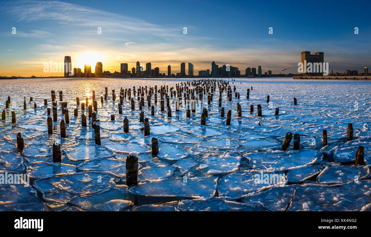 Tramonto sulla congelati Fiume Hudson con il legno vecchio palificazioni e vista sul centro città di Jersey, New Jersey Foto Stock