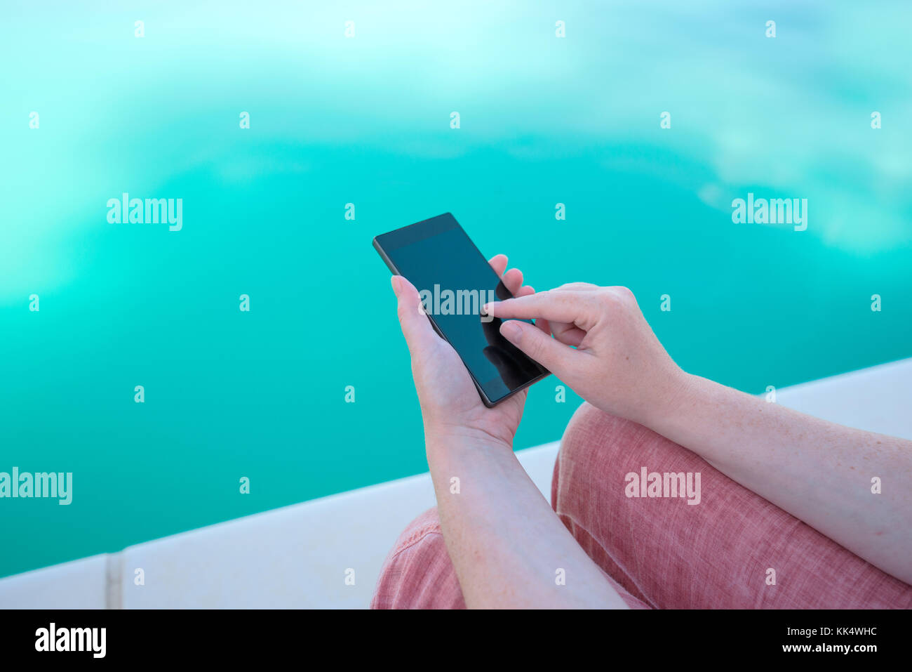 Utilizzando il telefono cellulare a bordo piscina, femmina mani tenendo lo smartphone Foto Stock