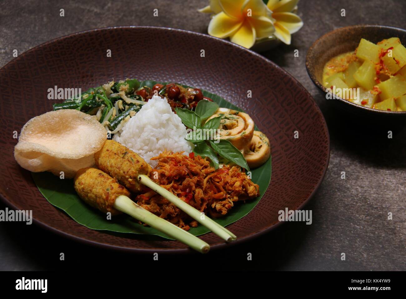 Il Nasi Campur Bali. Popolare il riso Balinesi piatto di riso al vapore con assortimento di piatti laterali, serviti insieme su una piastra con zuppa di curry a parte. Foto Stock