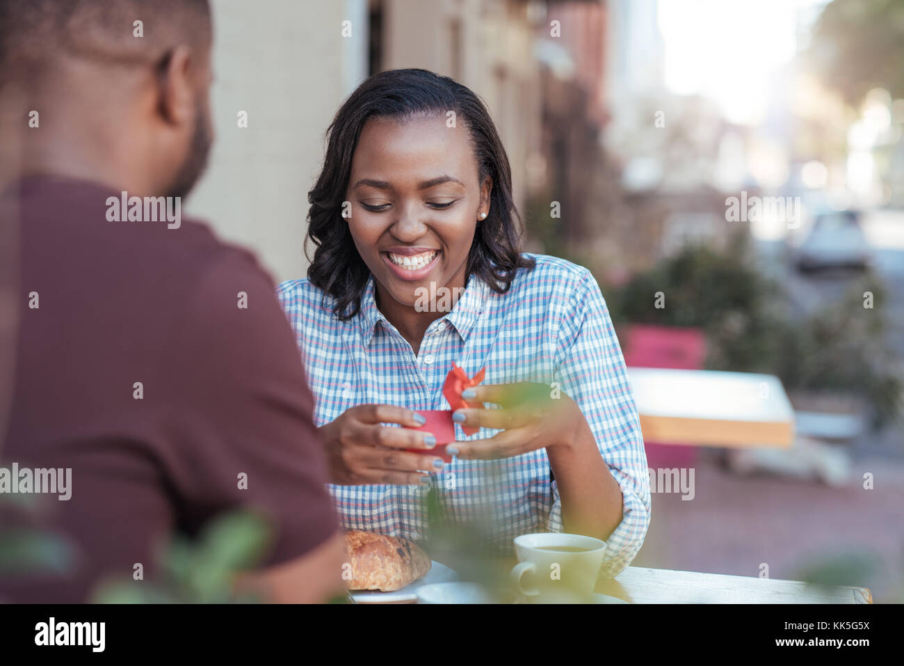 Sorridente giovane donna africana apre un regalo dal suo fidanzato Foto Stock