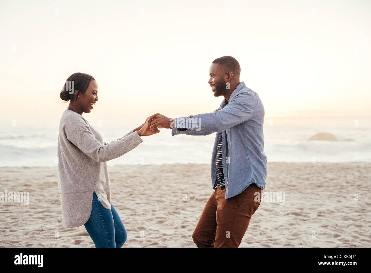 Sorridente giovane africano coppia danzante sulla spiaggia al tramonto Foto Stock