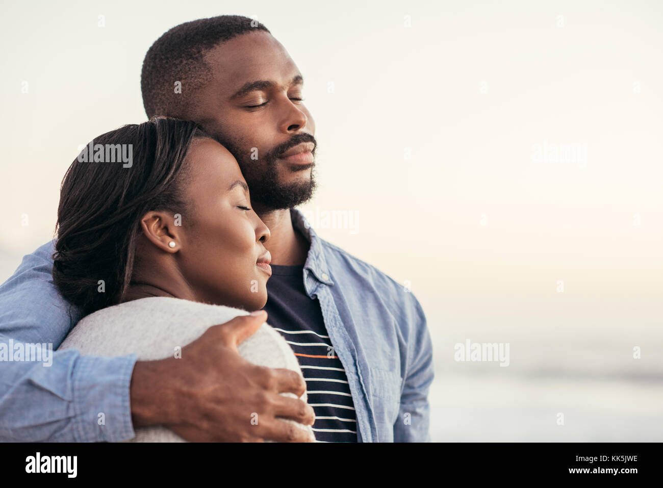 Contenuto coppia africana in piedi su una spiaggia che abbraccia ogni altro Foto Stock