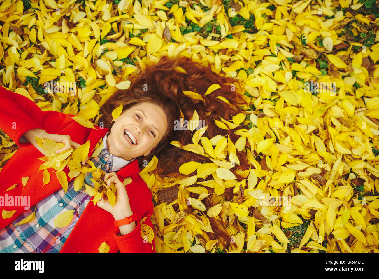 Bella ragazza felice che stabilisce in giallo le foglie di autunno. Foto Stock