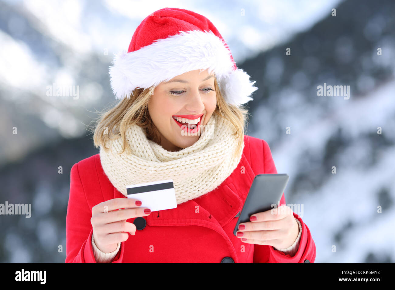 Acquirente sorpreso pagare on line con carta di credito e smart phone nel natale con una montagna innevata in background Foto Stock