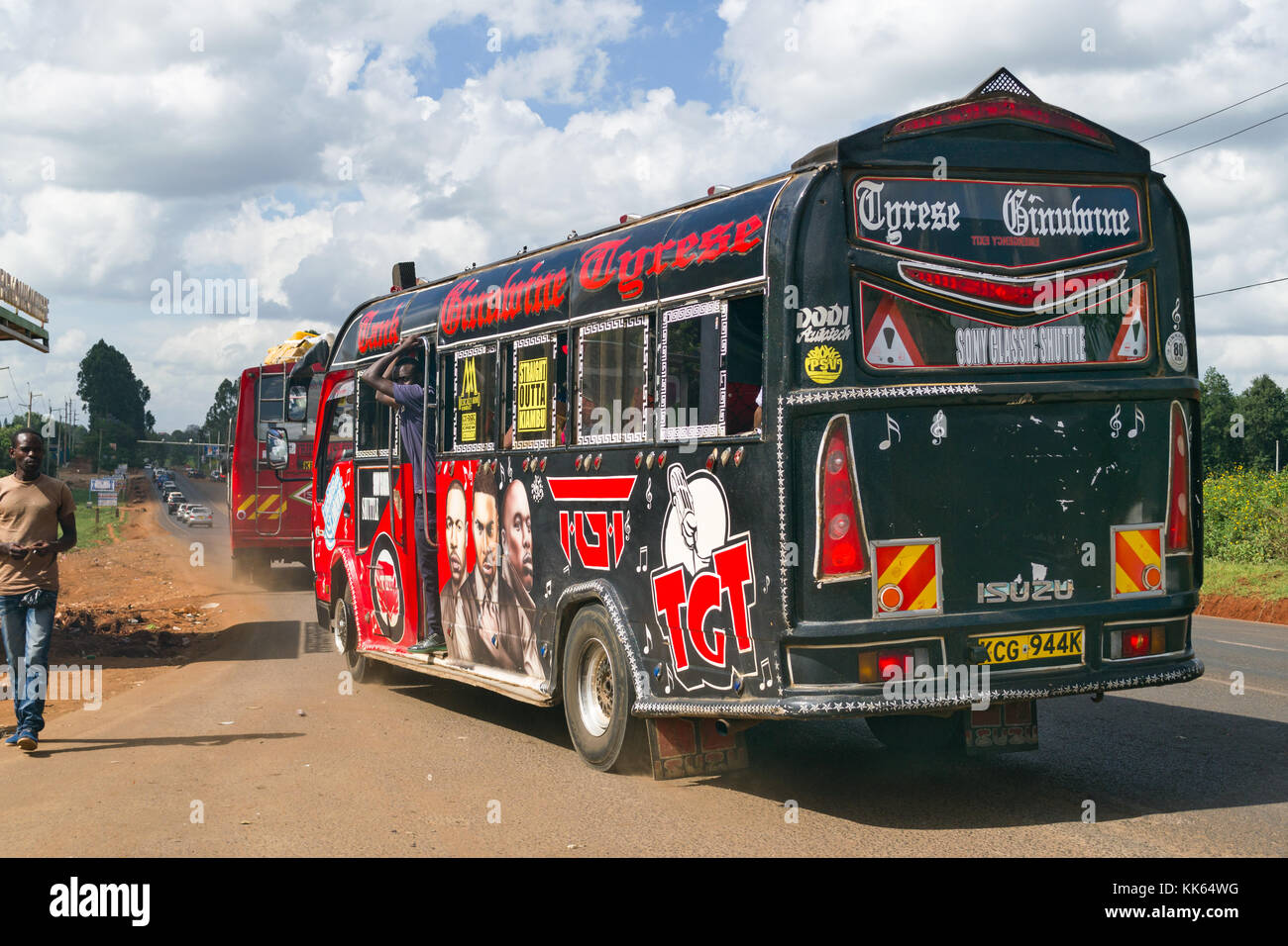 Un decorata luminosamente bus di grandi dimensioni tira a una fermata degli autobus con il conduttore in piedi in porta, Kenya, Africa orientale Foto Stock