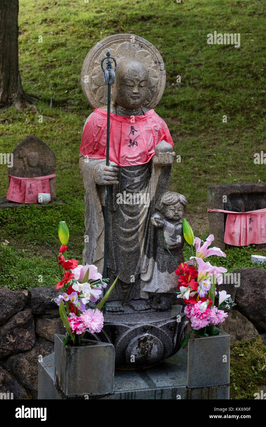 Nara - Giappone, 30 maggio 2017: tradizionale in pietra scolpita con jizo mantello rosso onorati e rispettati con fiori Foto Stock