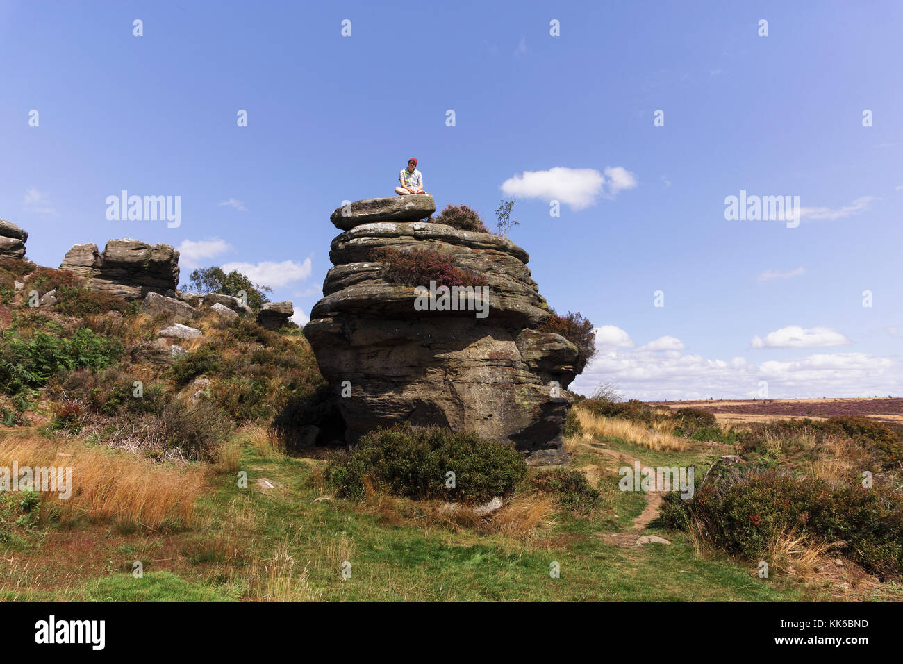 Un giovane uomo si siede sulla parte superiore di una formazione rocciosa a brimham rocks in North Yorkshire su una giornata d'estate. Foto Stock