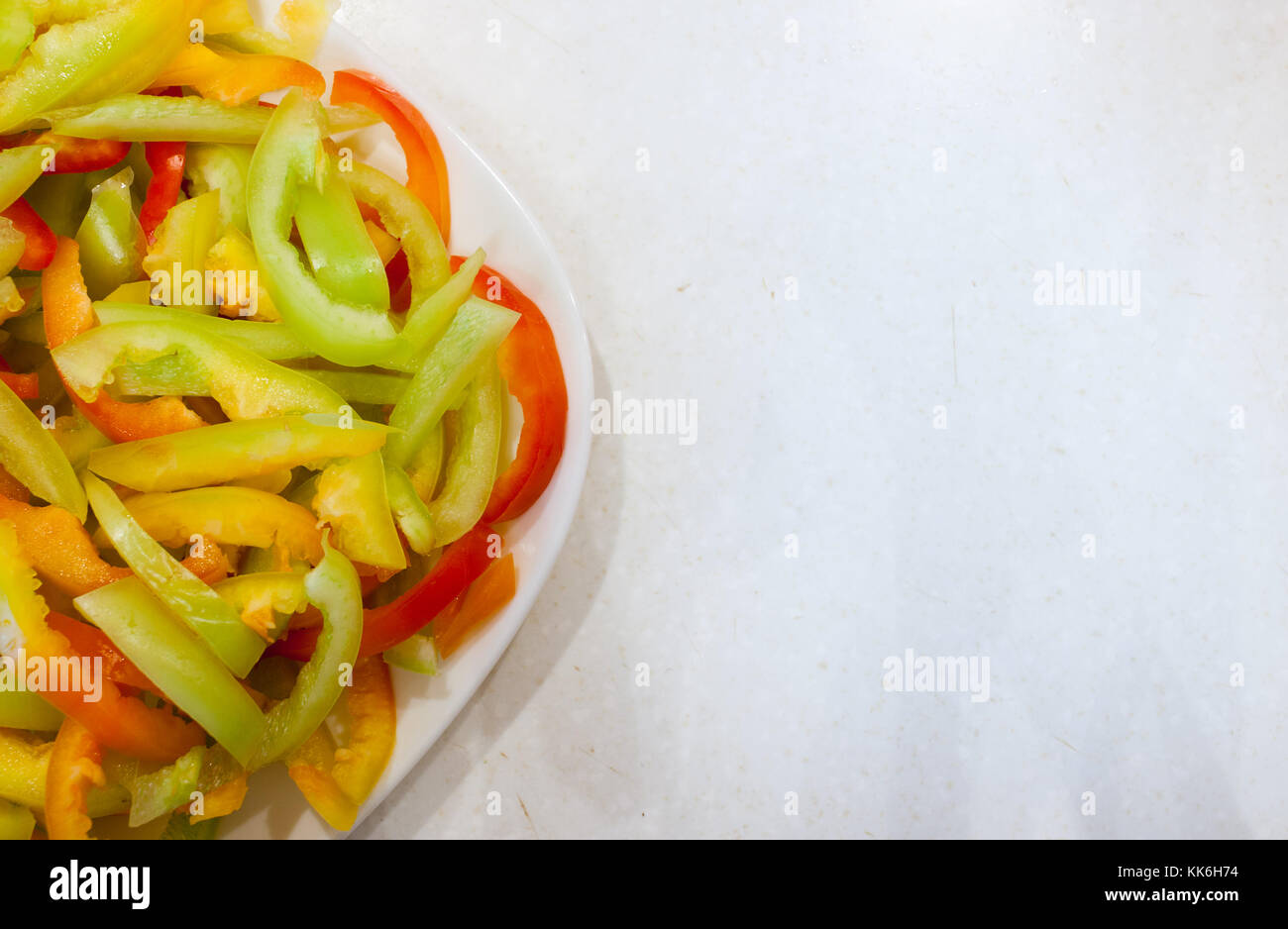 Parte della piastra bianca con fette di strisce longitudinali di ripe multi-peperoni colorati sul vecchio bianco tavola graffiato. Foto Stock