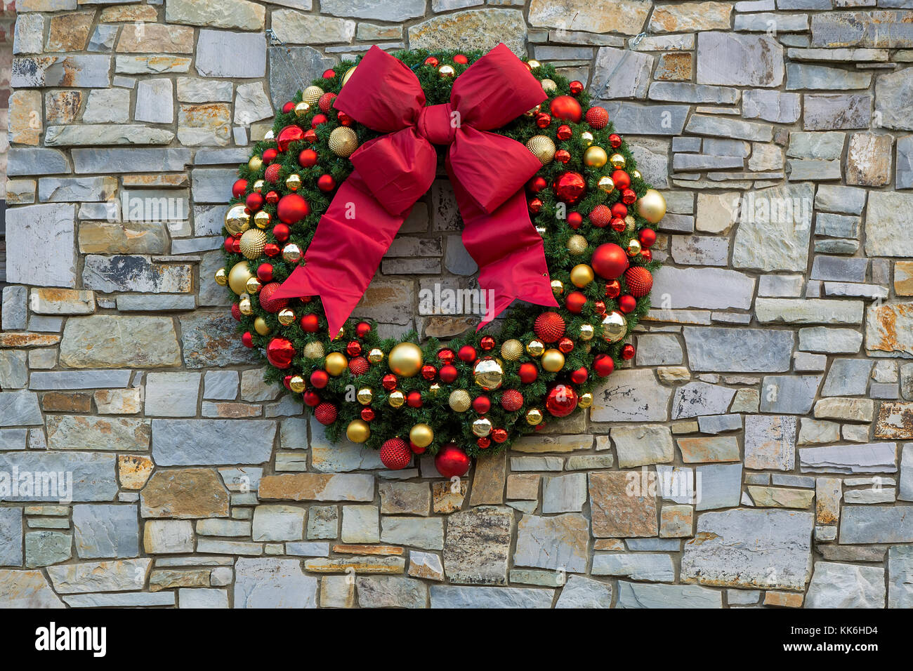 Vacanze di Natale ghirlanda con fiocco rosso nastri ornamenti appeso sulla roccia della parete di pietra Foto Stock