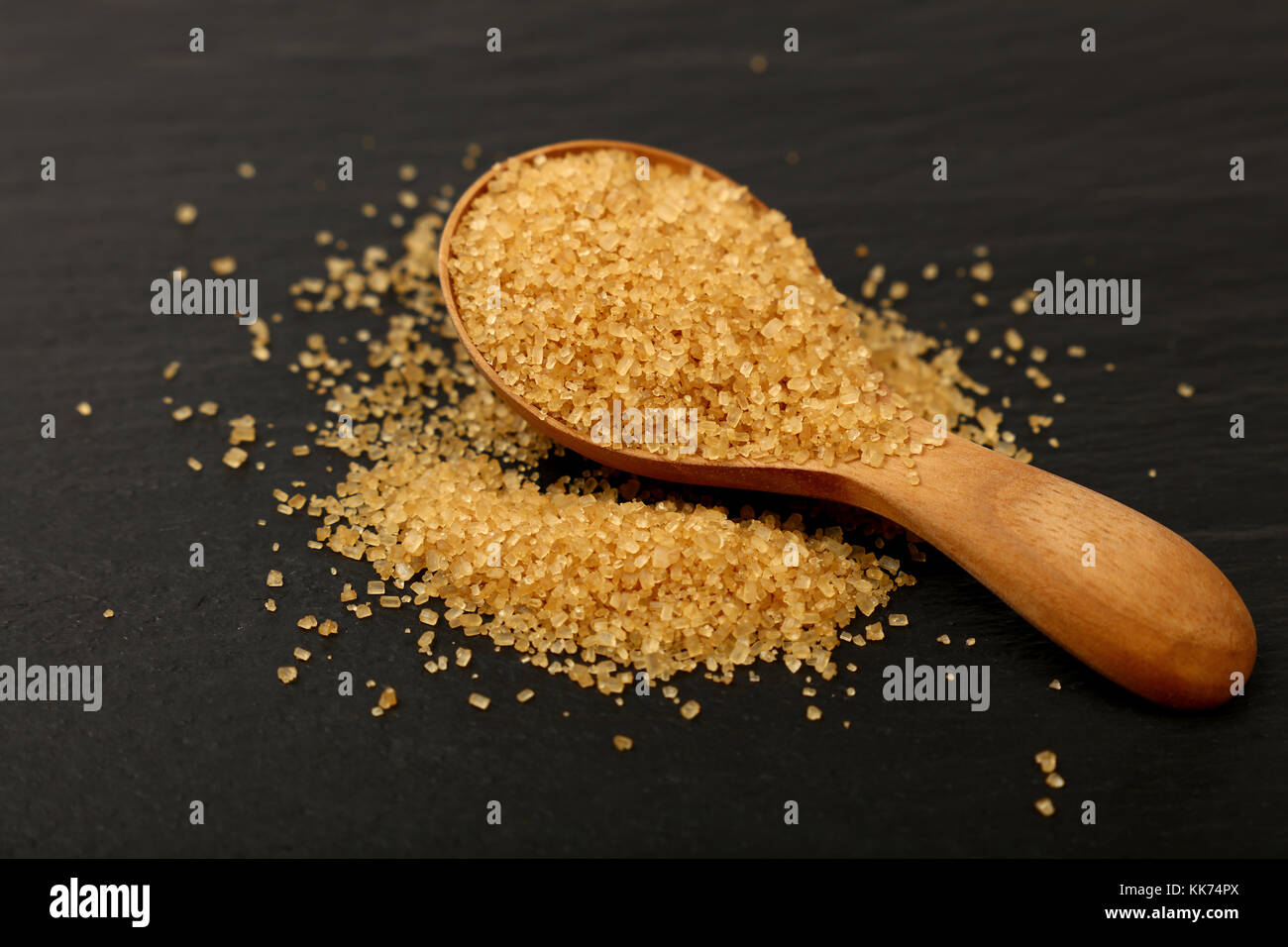 Chiudere uno scoop di legno cucchiaio colmo di marrone zucchero di canna sul nero ardesia bordo, a basso angolo di visione Foto Stock