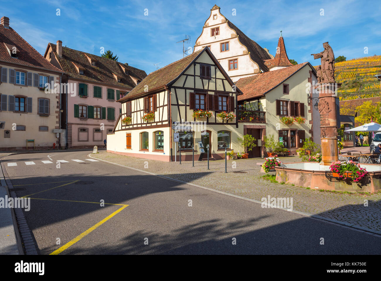Semi-case con travi di legno con fontana e vista sui vigneti, villaggio andlau, colline ai piedi delle montagne Vosges, sulla strada del vino dell'Alsazia, Francia Foto Stock