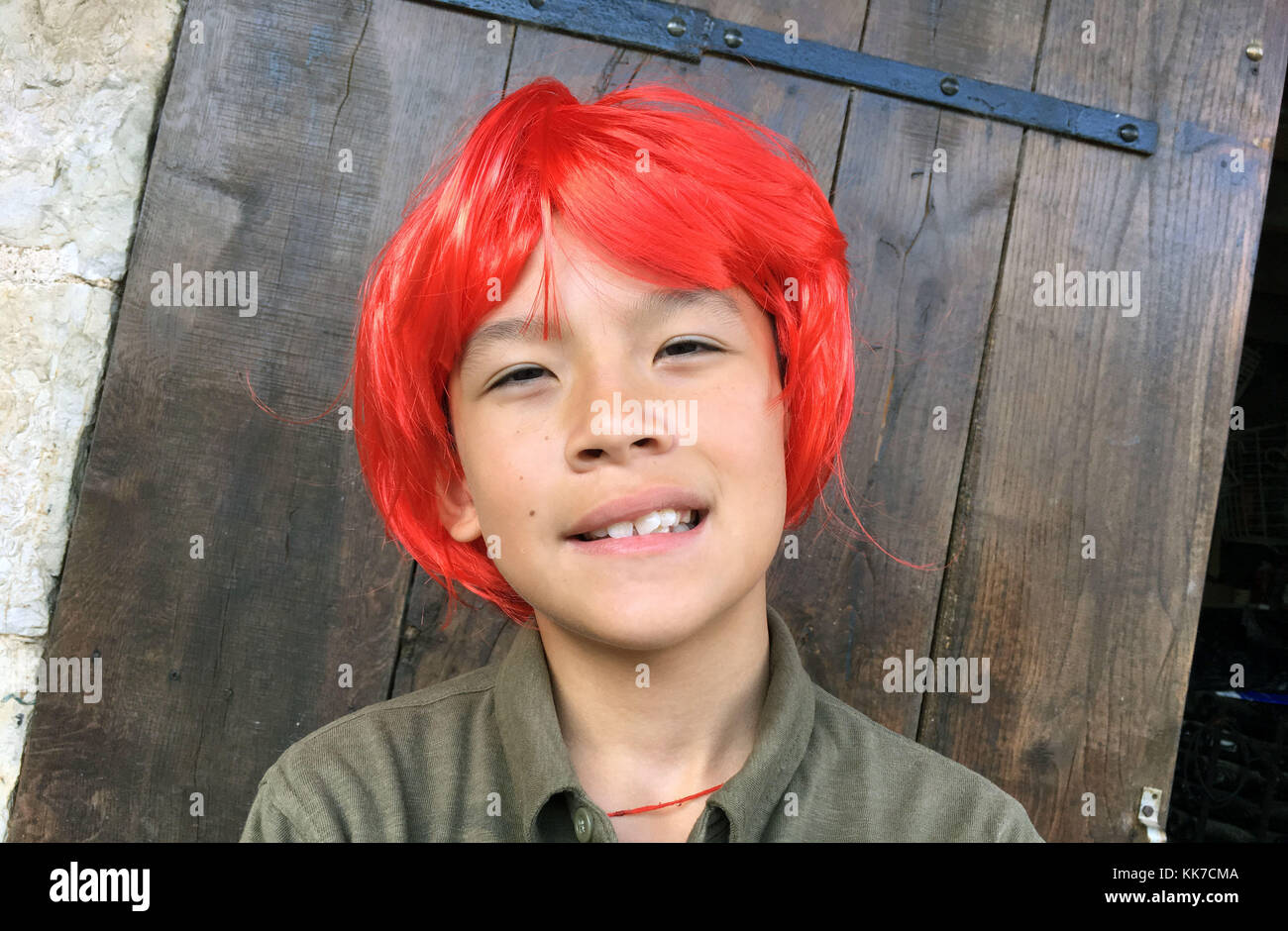 Giovane ragazzo asiatico sorridente con un ritratto rosso parrucca sullo schermo Foto Stock