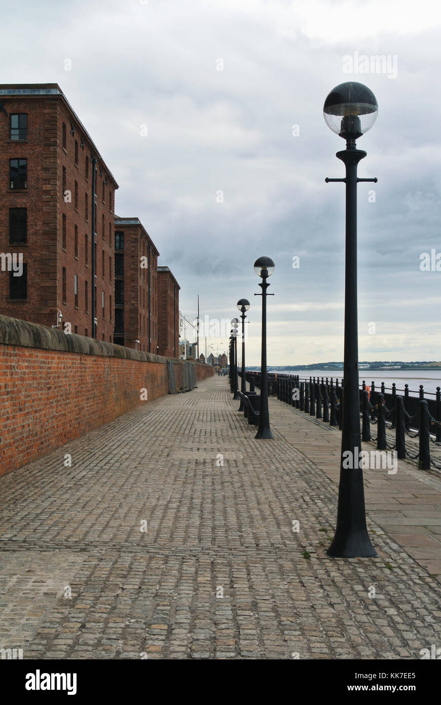 In acciottolato sentiero pavimentato passerella lungomare enbankment lungo il vecchio rosso mattone edifici storici a Liverpool Albert Dock. Foto Stock