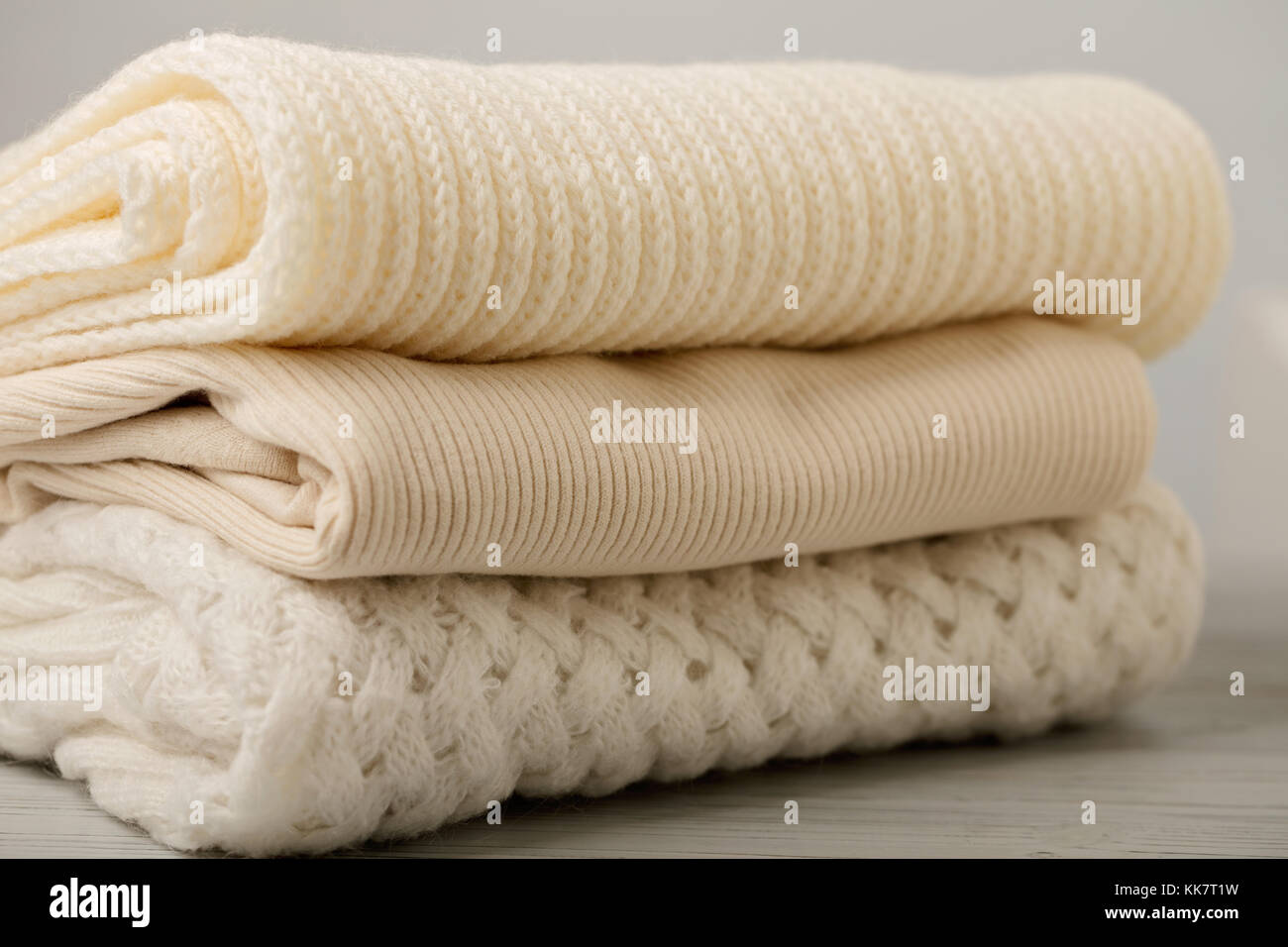 Pila di indumenti a maglia (maglioni, sciarpe, pullover) bianco e beige. messa a fuoco selettiva. Foto Stock