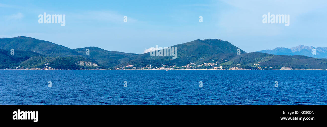 In orizzontale ampia foto con la costa di Isola d'elba. La costa è costituita da montagne coperte dalla macchia verde e alberi. il cielo è blu con poche nuvole. Foto Stock