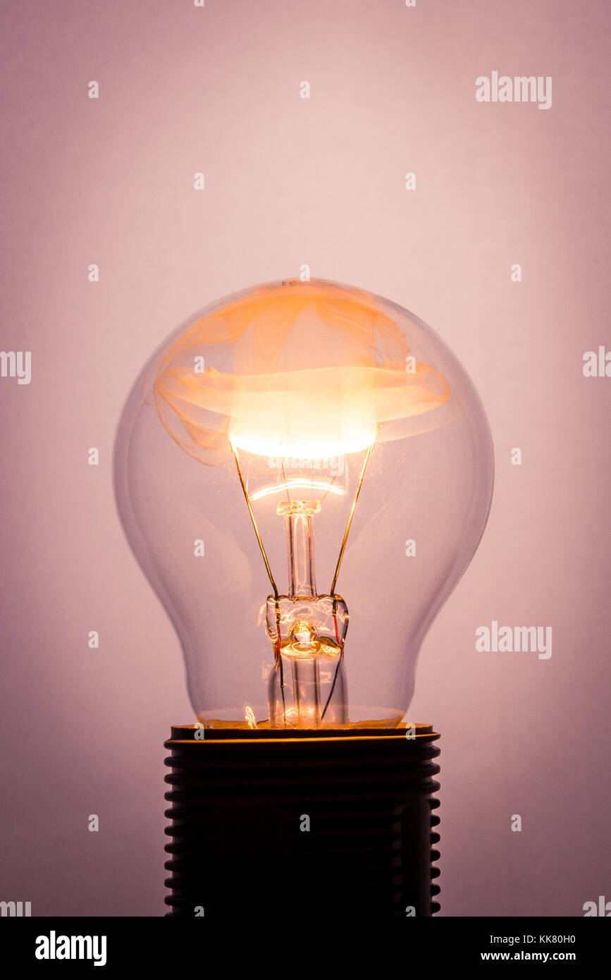 Foto verticale del bulbo di vetro che è posizionato nel connettore a presa con fiamma arancione all'interno. Il filo è in fiamme e fumo e particals stanno riempiendo i Foto Stock