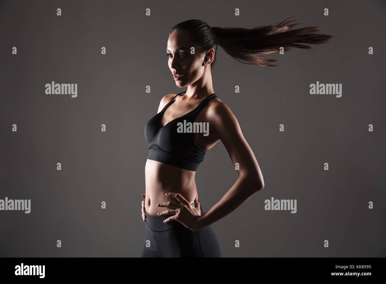 Ritratto di un giovane attraente donna fitness in piedi con le mani sui fianchi isolate su uno sfondo grigio Foto Stock