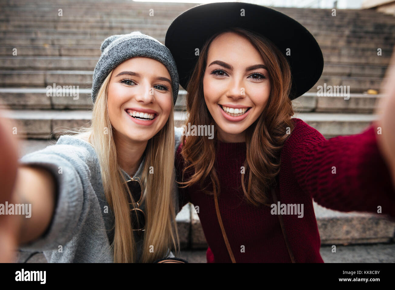 Ritratto di due sorridendo felice ragazze prendendo un selfie mentre è seduto su una scalinata e guardando la fotocamera all'aperto Foto Stock