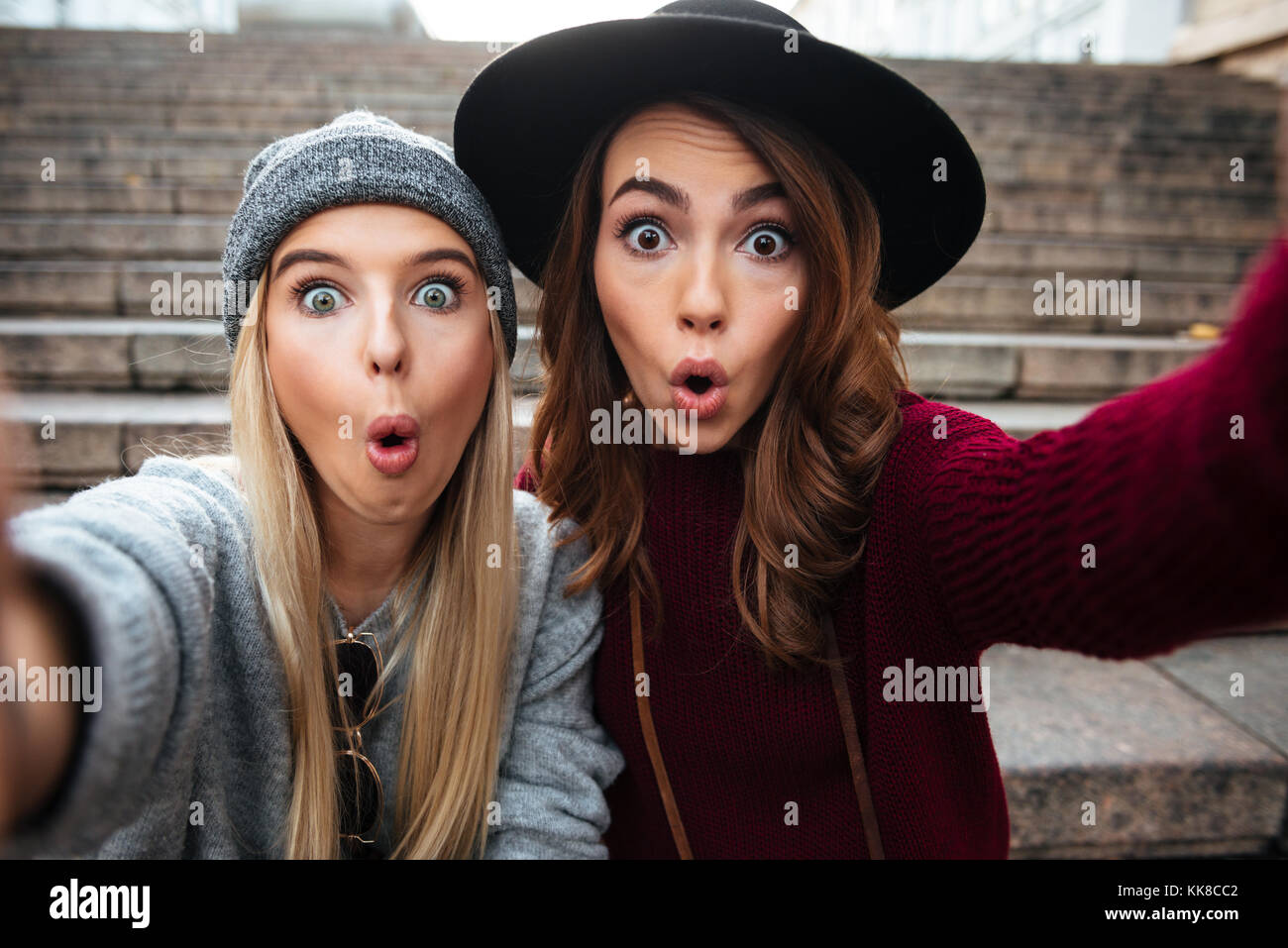 Ritratto di due divertenti le giovani ragazze prendendo un selfie mentre è seduto su una scalinata e faccia gesticolando all'aperto Foto Stock