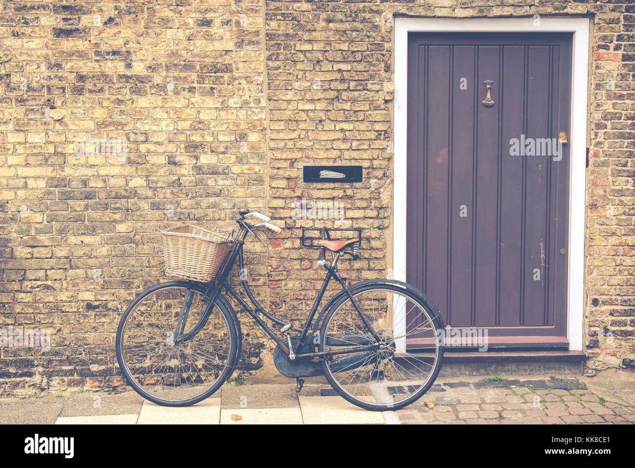 Vintage bicicletta retrò con cesto in vimini parcheggiato di fronte a una casa porta anteriore opaca. Foto Stock