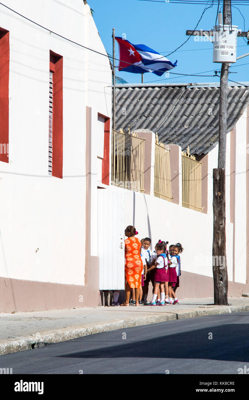 I bambini della scuola elementare e la loro insegnante sotto una bandiera cubana al di fuori della loro scuola a Cienfuegos, Cuba Foto Stock