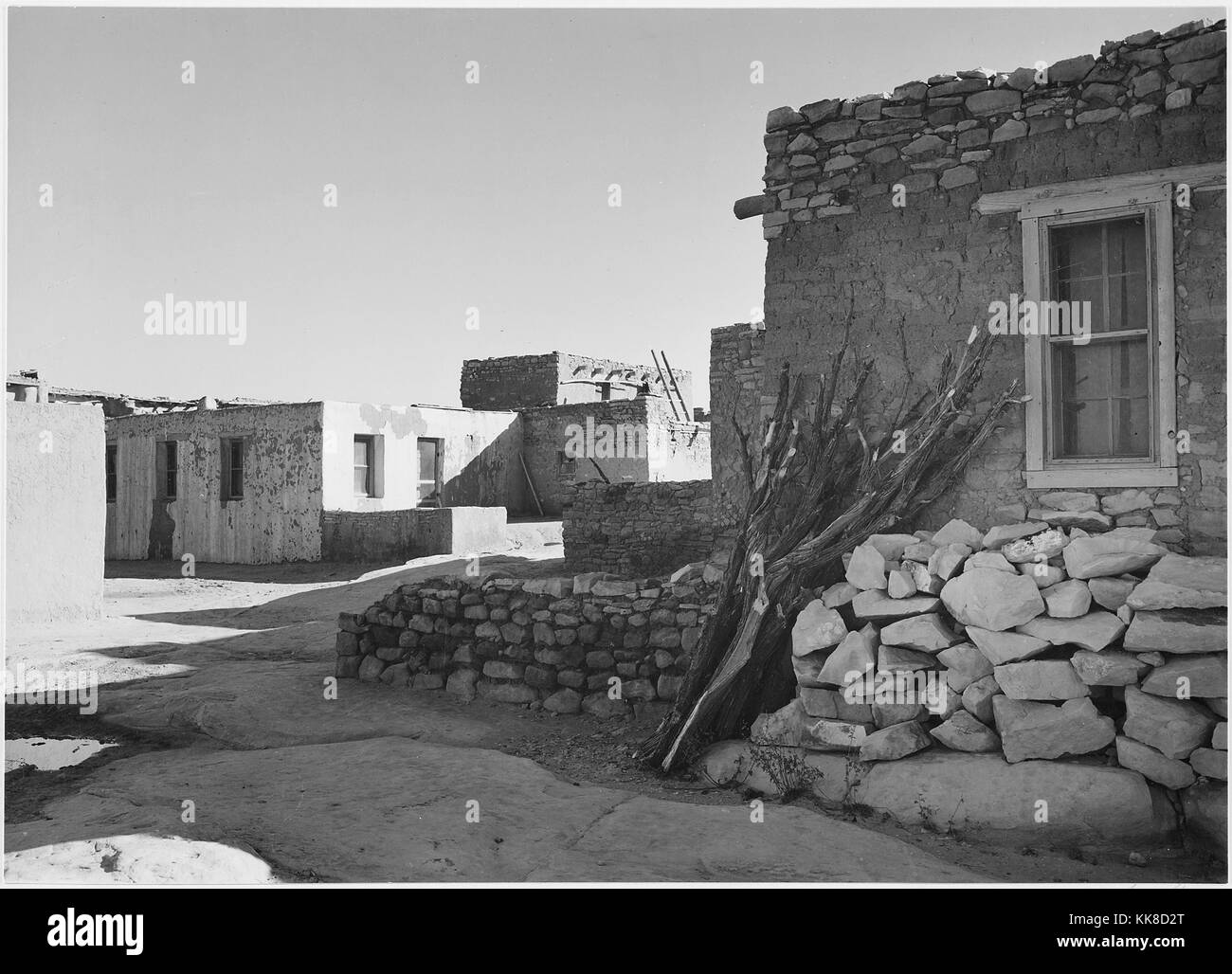 Una fotografia in bianco e nero di diverse abitazioni con una corsa su strada tra di loro, le case sono fatte di pietra e adobe, travi utilizzati per supportare i massimali possono essere visti sporgenti da alcuni dei tetti, l'immagine proviene da una serie di fotografie noto come il progetto murale di Ansel Adams, fu commissionato dal Servizio del parco nazionale nel 1941 per creare un murale fotografico per il dipartimento dell'interno edificio in Washington DC, il progetto è giunto a termine a causa della Seconda Guerra Mondiale, la casa è parte di Acoma Pueblo e è stata abitata per oltre 800 anni, Acoma Indian Reservation, New Mexic Foto Stock