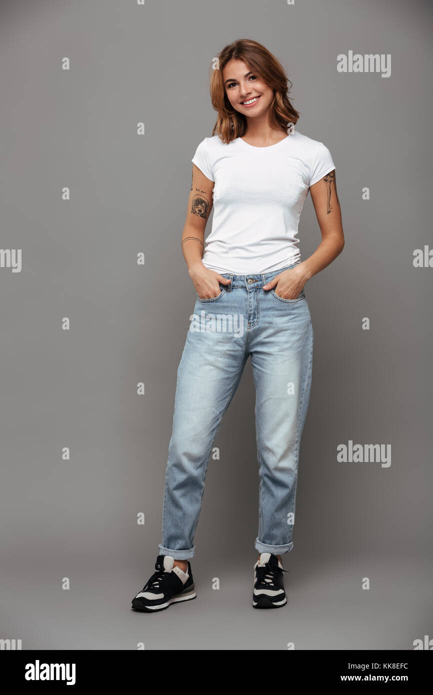 Lunghezza completa foto di carino brunette donna con mani in tasca alla  moda da indossare jeans mom e white tshirt, guardando la telecamera,  isolato su bianco b Foto stock - Alamy