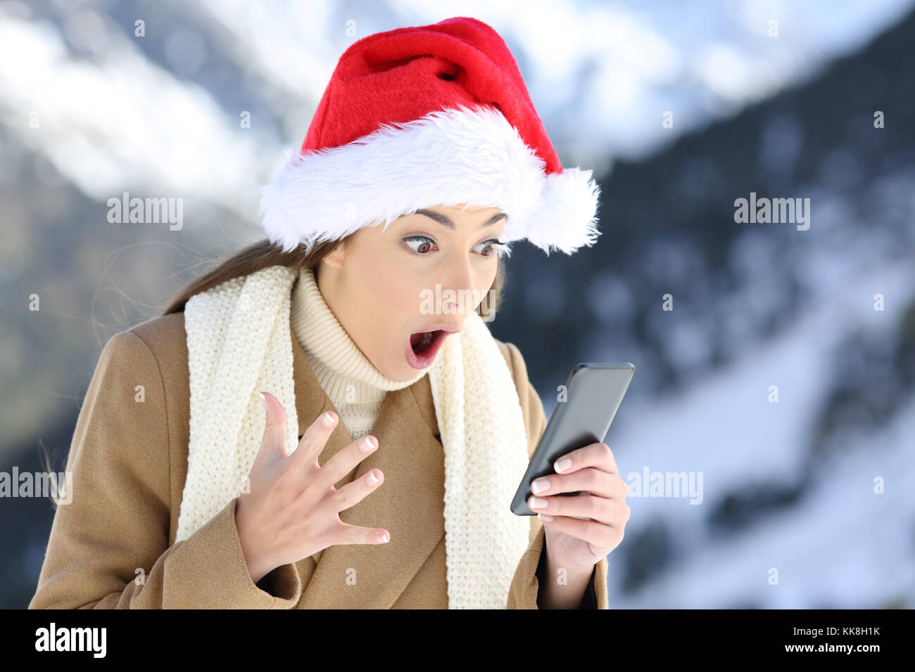 Stupiti lettura della ragazza on line news a Natale con una montagna innevata in background Foto Stock