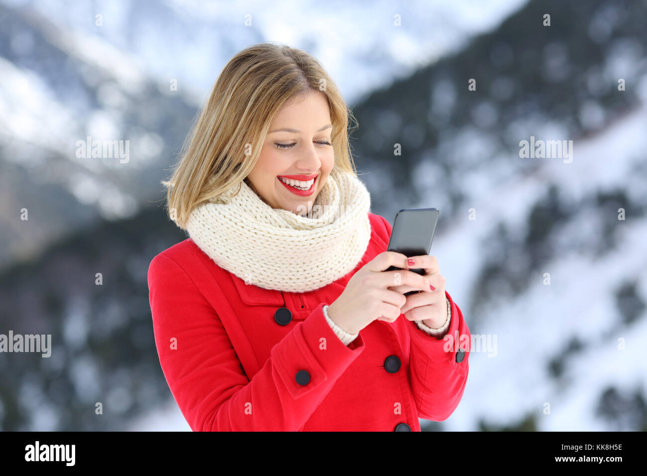 Woman in Red utilizzando smart phone in inverno con una montagna innevata in background Foto Stock