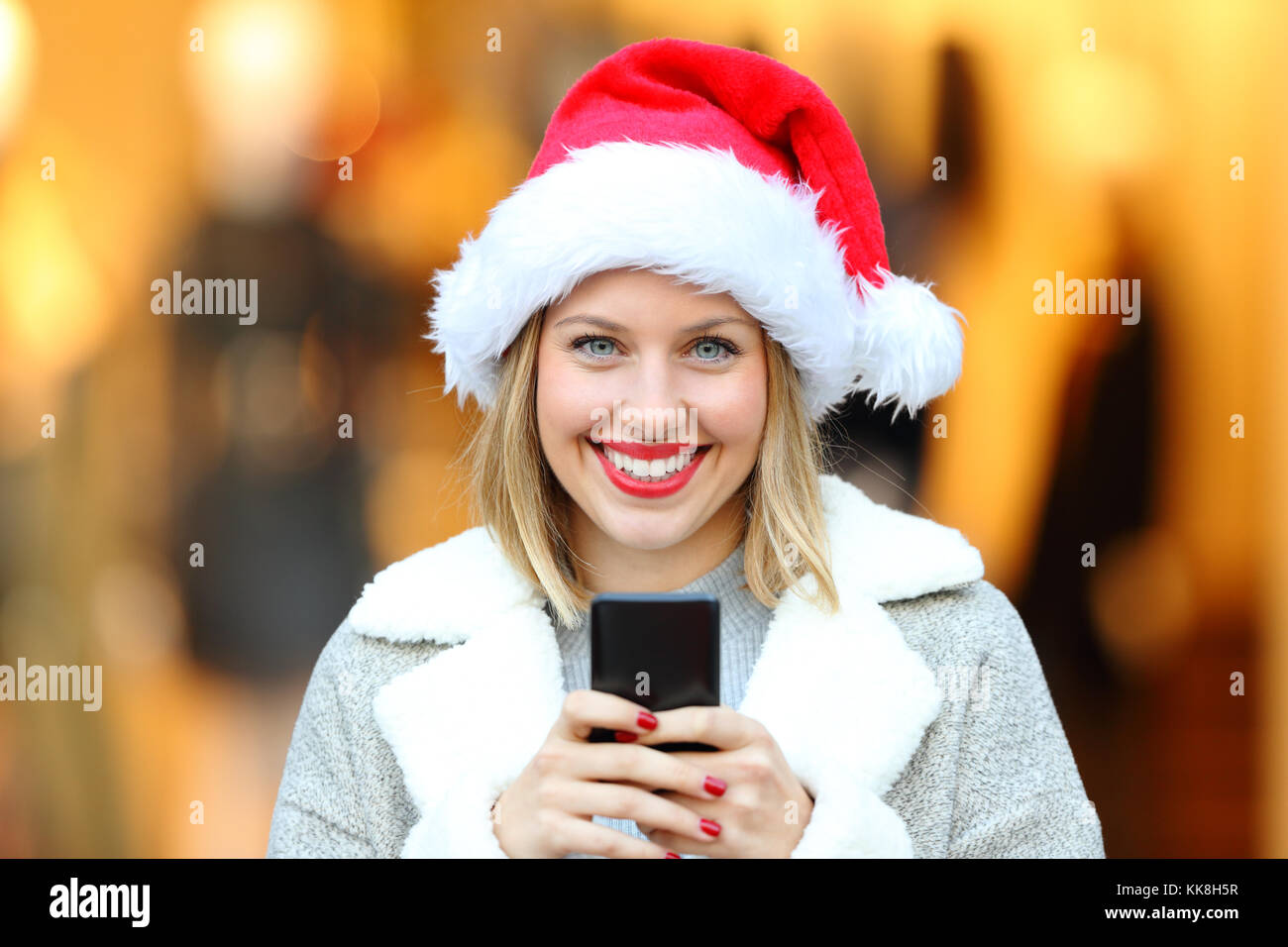 Vista frontale il ritratto di una bella donna che indossa santa claus hat su vacanze di Natale azienda smart phone su strada Foto Stock