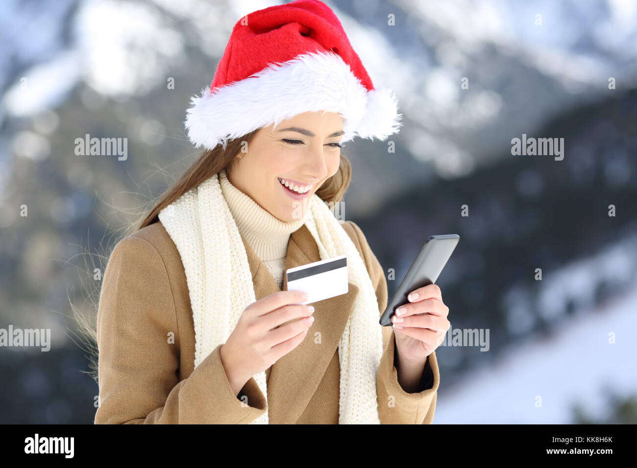 Ritratto di una donna che indossa santa claus hat sul Natale il pagamento on line con carta di credito e smart phone con una montagna innevata in background Foto Stock