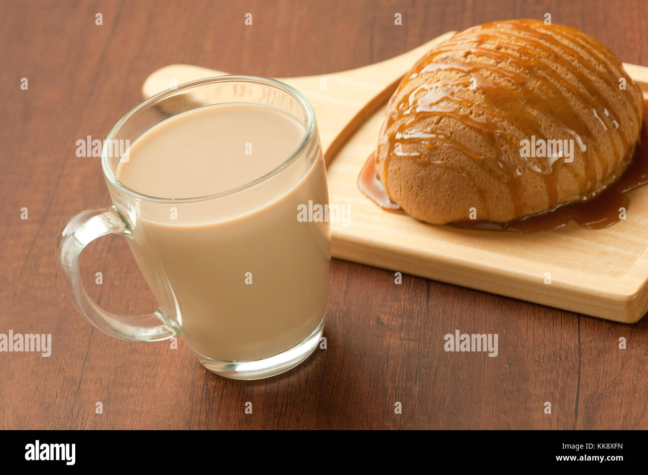 Pane spruzzata con miele su un piatto di legno e un bicchiere di latte shake Foto Stock