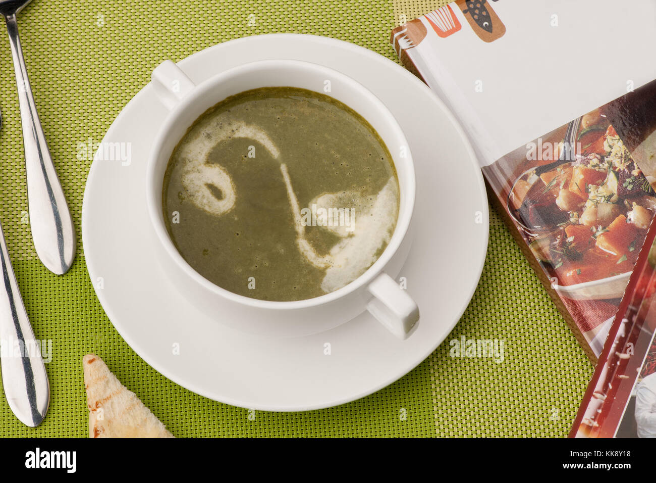 La zuppa in una ciotola bianca con un libro e posate su una tovaglia verde Foto Stock