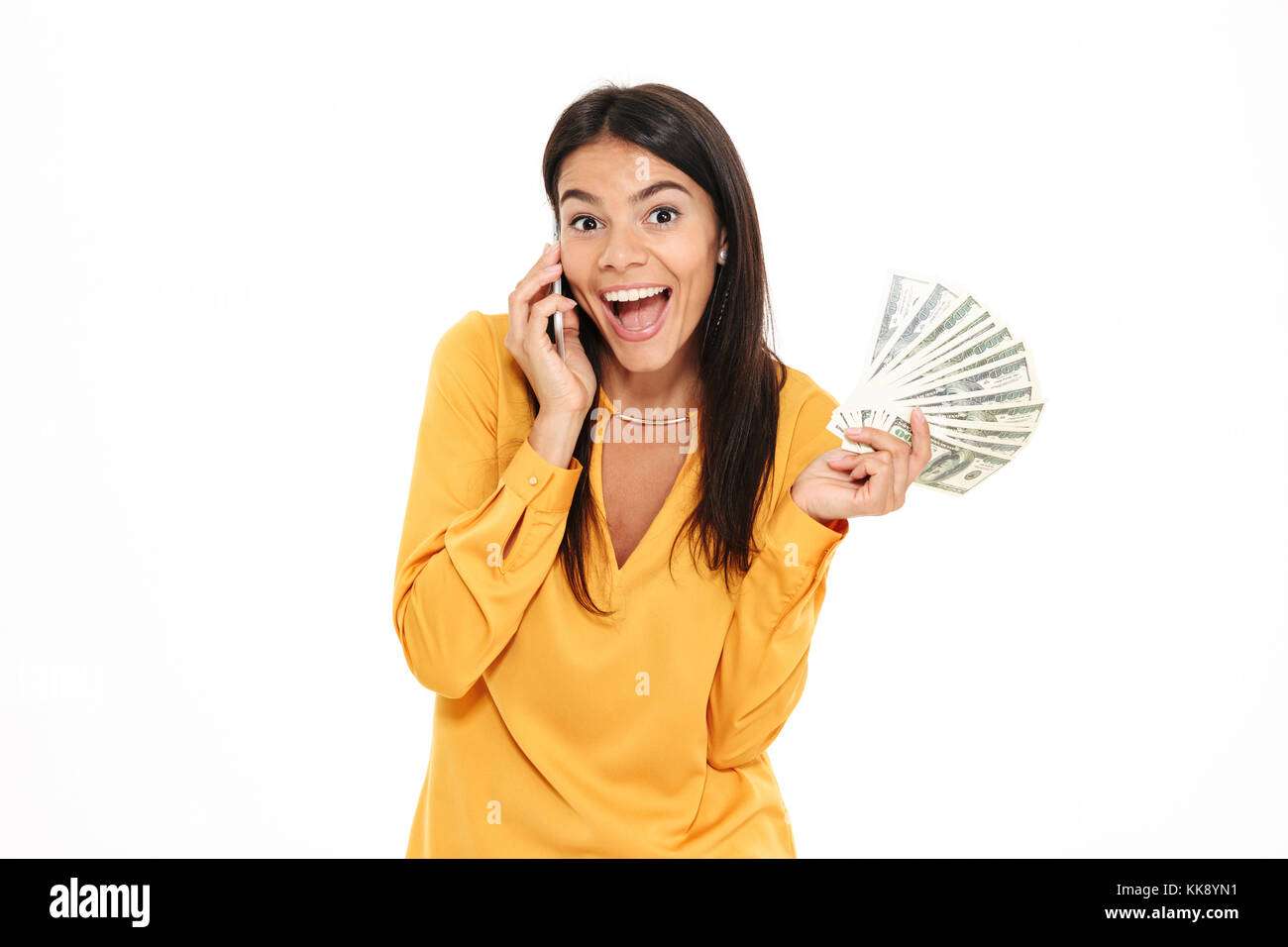 Ritratto di un felice Excited donna parlando al telefono cellulare mantenendo mucchio di soldi banconote isolate su sfondo bianco Foto Stock