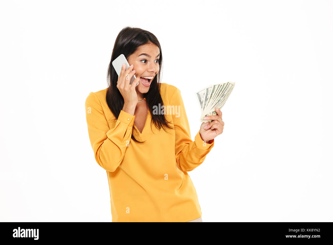 Ritratto di una lieta sorpresa donna parlando al telefono cellulare mantenendo mucchio di soldi banconote isolate su sfondo bianco Foto Stock