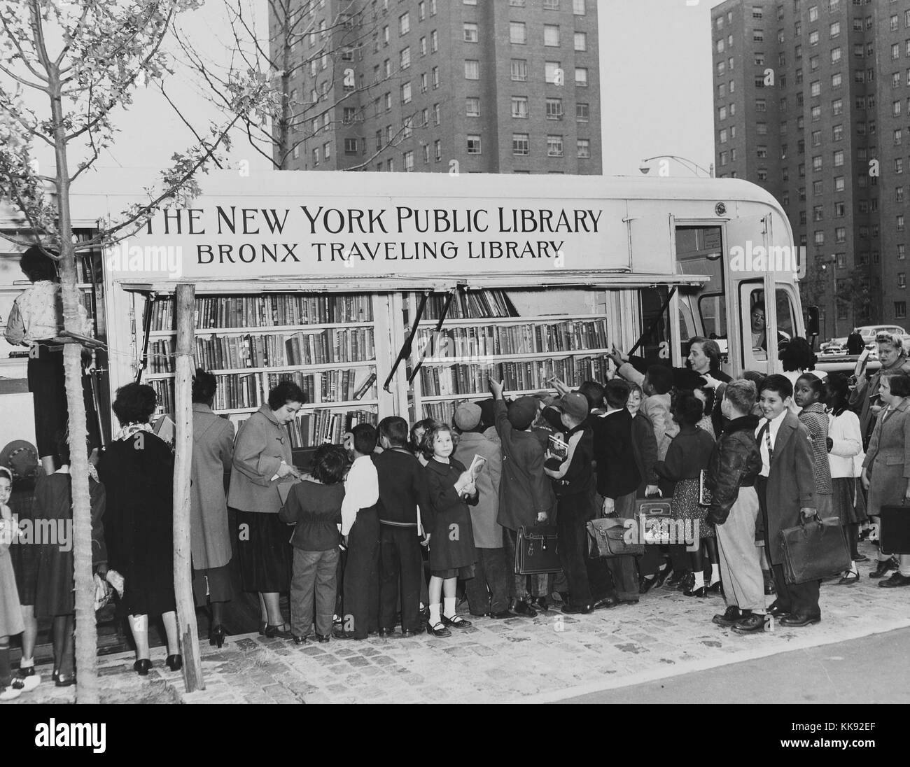 Fotografia in bianco e nero che mostra un folto gruppo di giovani bambini e alcuni adulti, a bookmobile contrassegnati 'New York Public Library, Bronx viaggia Library', Bronx, New York, New York, 1954. Dalla Biblioteca Pubblica di New York. Foto Stock