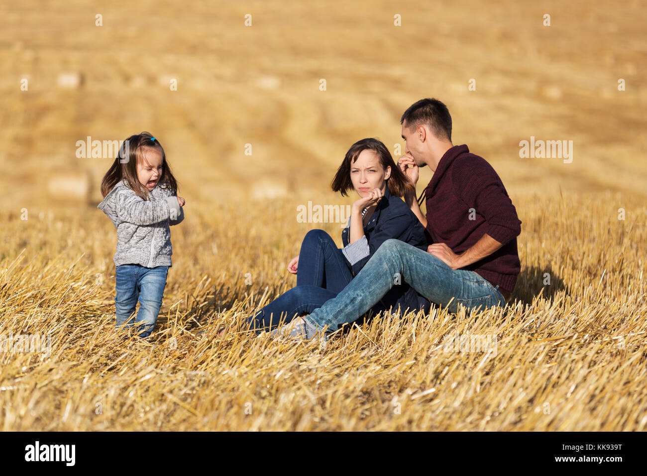 Felice famiglia giovane con 2 anno di età ragazza seduta sul terreno nel campo di raccolto Foto Stock