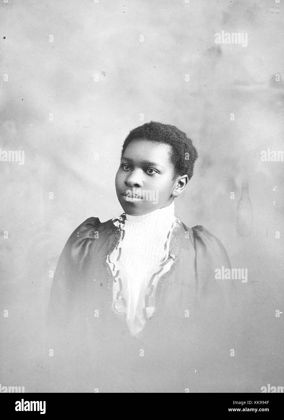 Un ritratto fotografico di una giovane donna che indossa un colore scuro abito che è accentato con il materiale bianco per creare l'aspetto di un collo chino linea, ella si pone guardando verso il suo diritto ad un angolo di 45 gradi rispetto alla telecamera, 1900. Dalla Biblioteca Pubblica di New York. Foto Stock