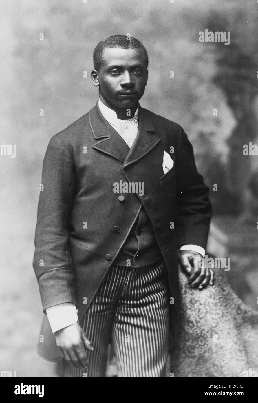 Seppia ritratto in studio di un afro-americano di uomo, tre quarti di  lunghezza, vestito in camicia, giubbotto, cravatta e pantaloni a strisce,  1900. Dalla Biblioteca Pubblica di New York Foto stock -