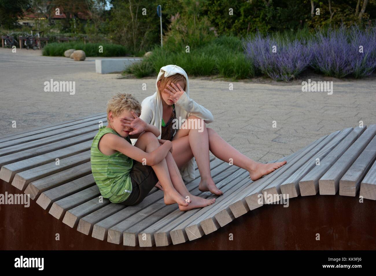 Due bambini di sedersi sul banco ondulato, tenere le mani prima di faccia Foto Stock