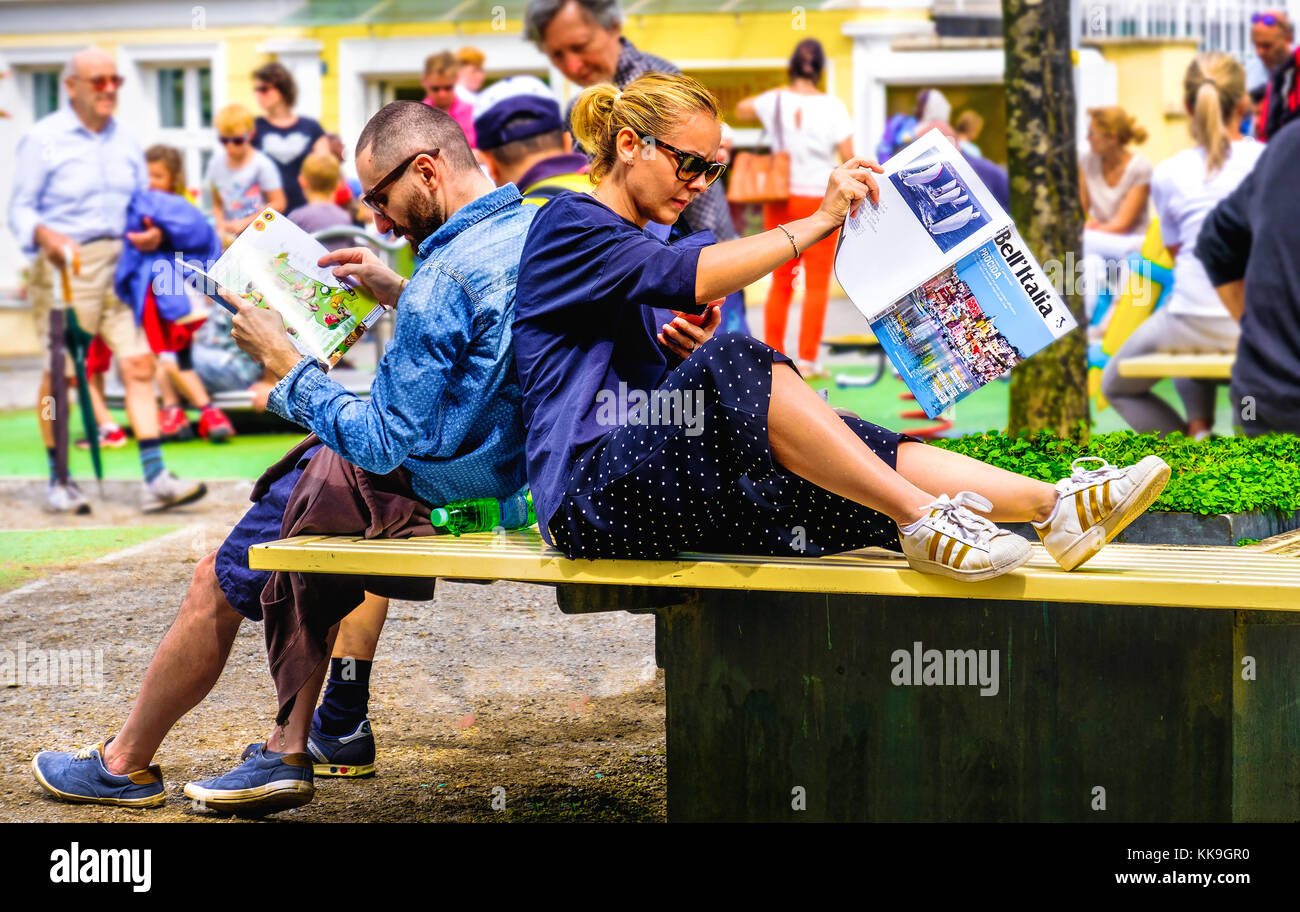 Coppia giovane seduto sul banco di città pianificazione viaggio in Italia la lettura di riviste di viaggi in Merano, Italia, 11 Ago 2017 Foto Stock