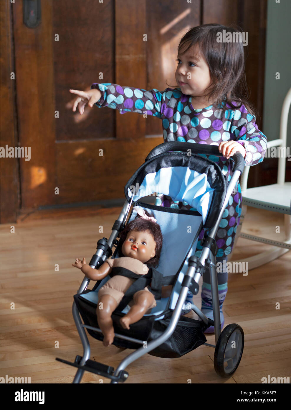Una bambina di 2 anni spinge la bambola in uno stroller. Foto Stock