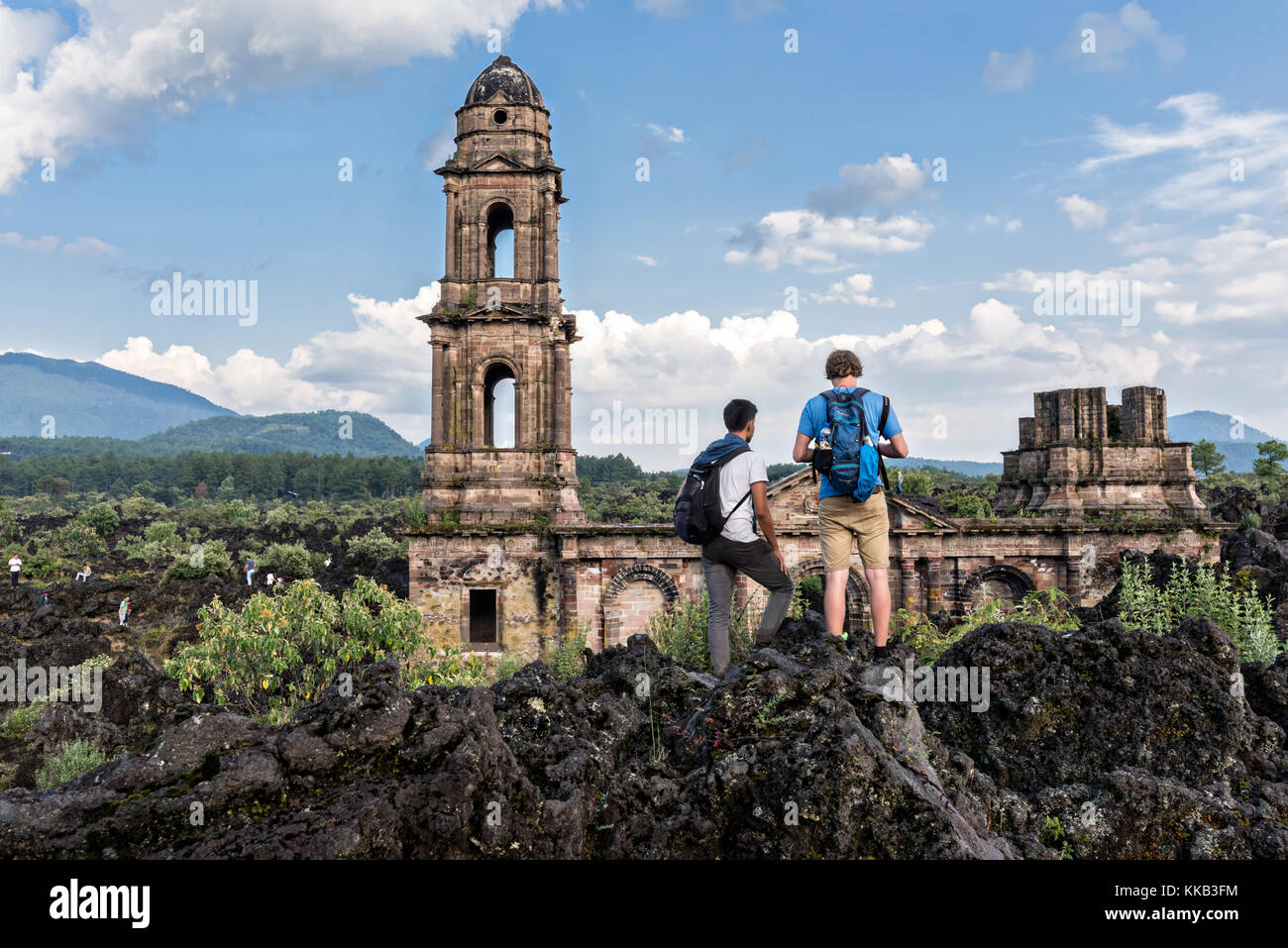 I turisti si aggrappano intorno al campanile di San Juan Parangaricutiro chiesa che si erge da un mare di roccia lavica secca nel remoto villaggio di San Juan Parangaricutiro, Michoacan, Messico. Questa chiesa è l'unica struttura rimasta sepolta nell'eruzione di otto anni del vulcano Paricutin che consumò due villaggi nel 1943 e coprì la regione in lava e cenere. Foto Stock