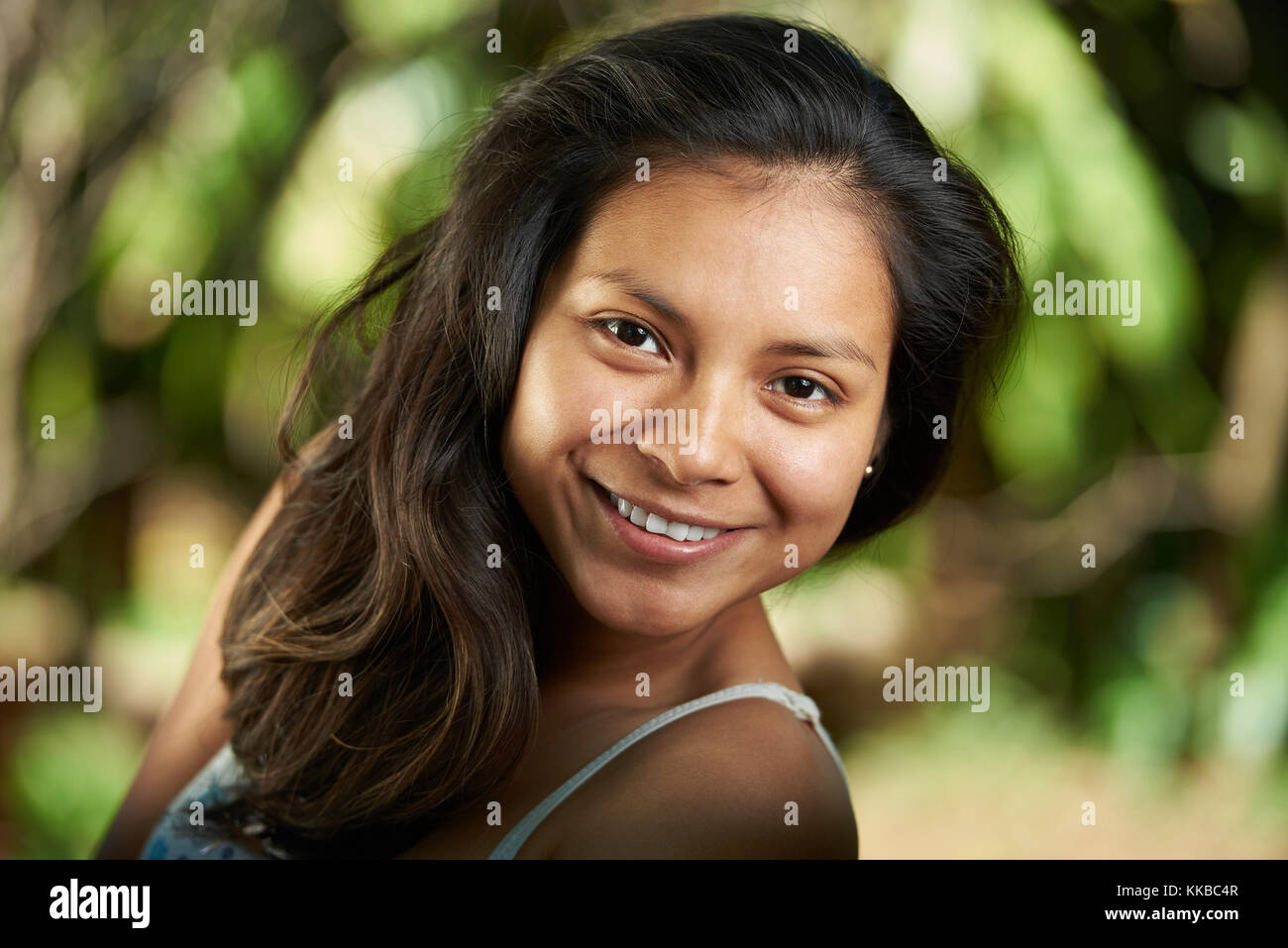 Attraente sorridente giovane donna ispanica headshot ritratto su sfondo naturale senza trucco Foto Stock