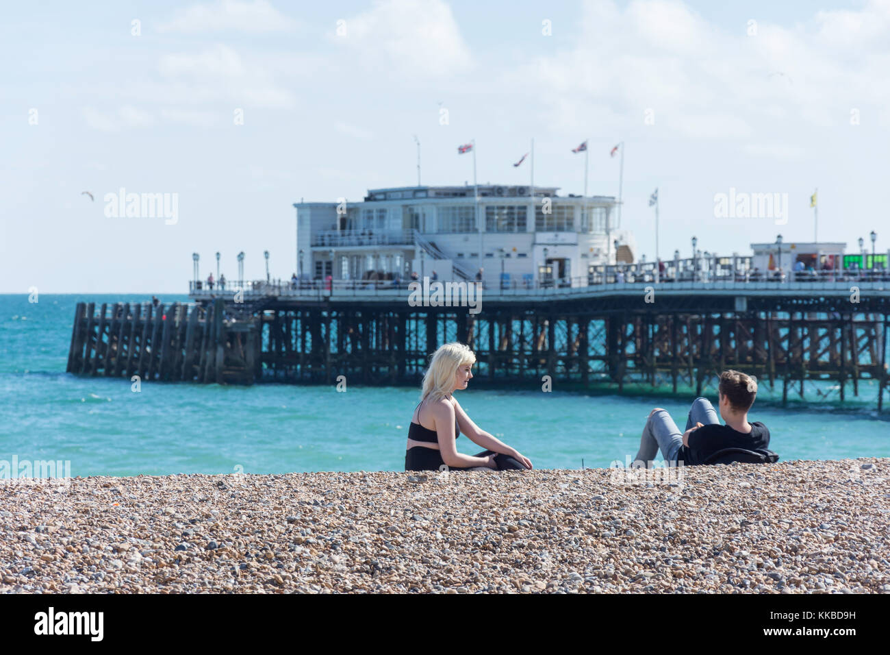Coppia giovane sulla spiaggia con Worthing Pier dietro, Worthing, West Sussex, in Inghilterra, Regno Unito Foto Stock