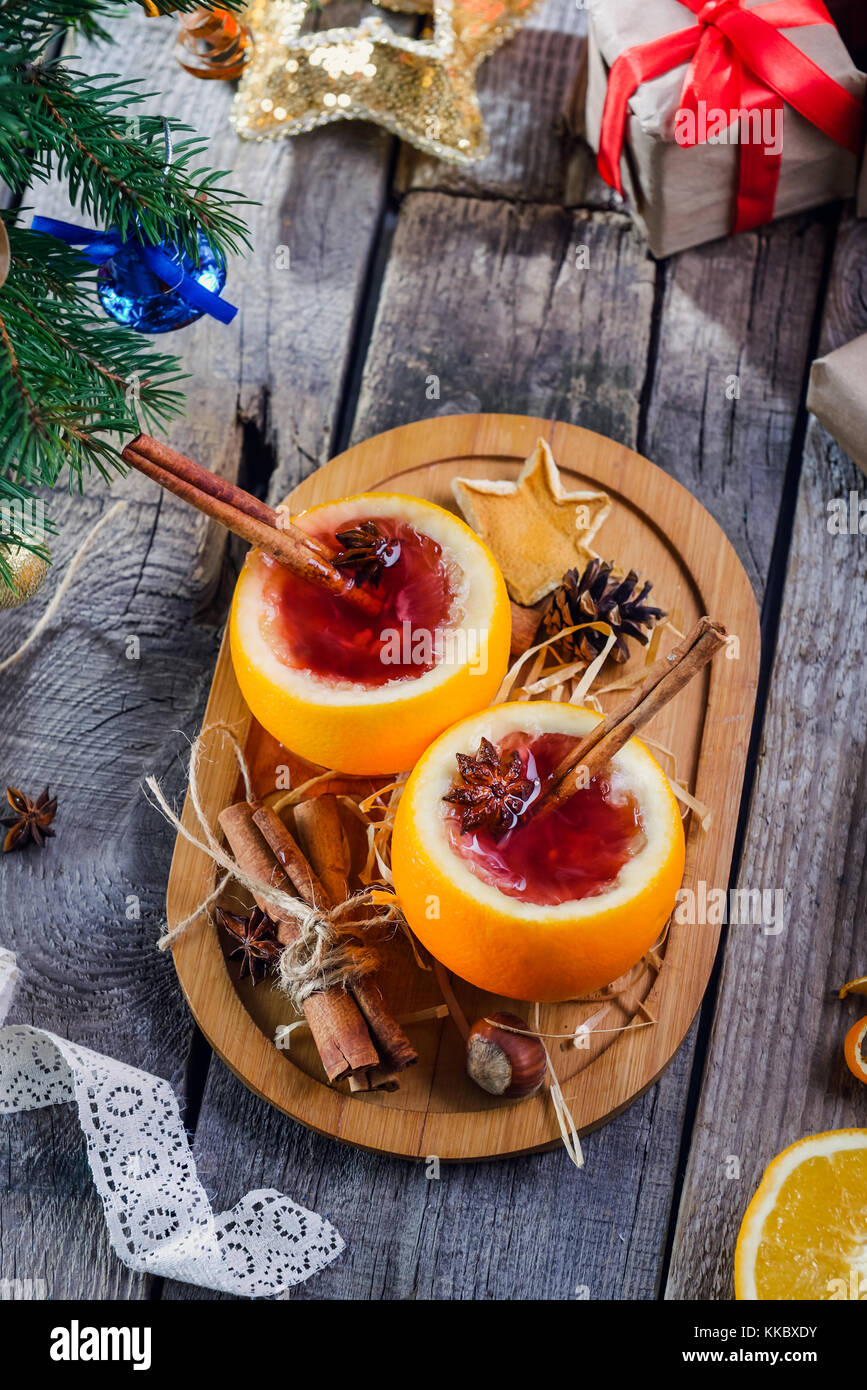 Natale vin brulé - insoliti servita in arancione. calda inverno drink con frutti di bosco, arancia, spezie, cannella sul vecchio tavolo in legno con doni, Abete rami, Foto Stock